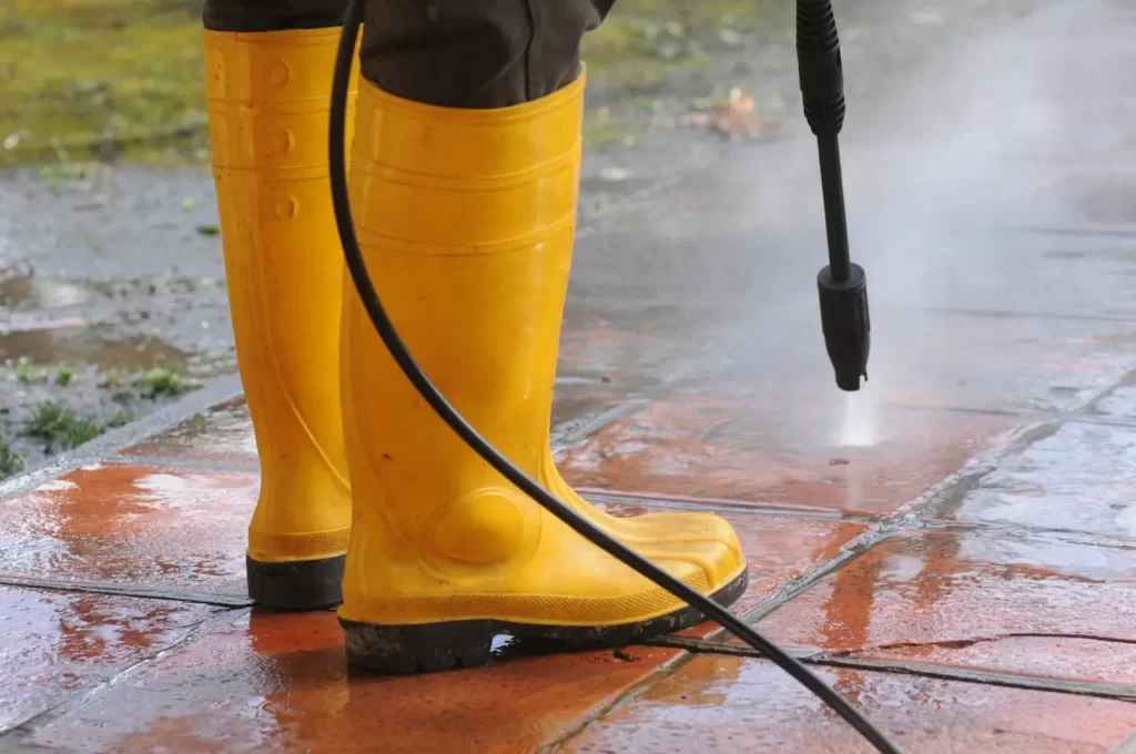 persona vestida botas goma amarilla boquilla agua alta presion limpiando suciedad baldosas - Caribbean Cleaning Srq