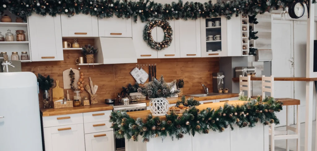 vistas la cocina moderna con alacenas blancas y mesa marron decorada con ramas de abeto verde natural y corona de navidad decoraciones de navidad - Caribbean Cleaning Srq